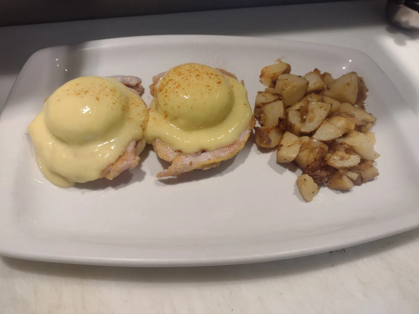 Two eggs benedict with hollandaise and a pile of home fries